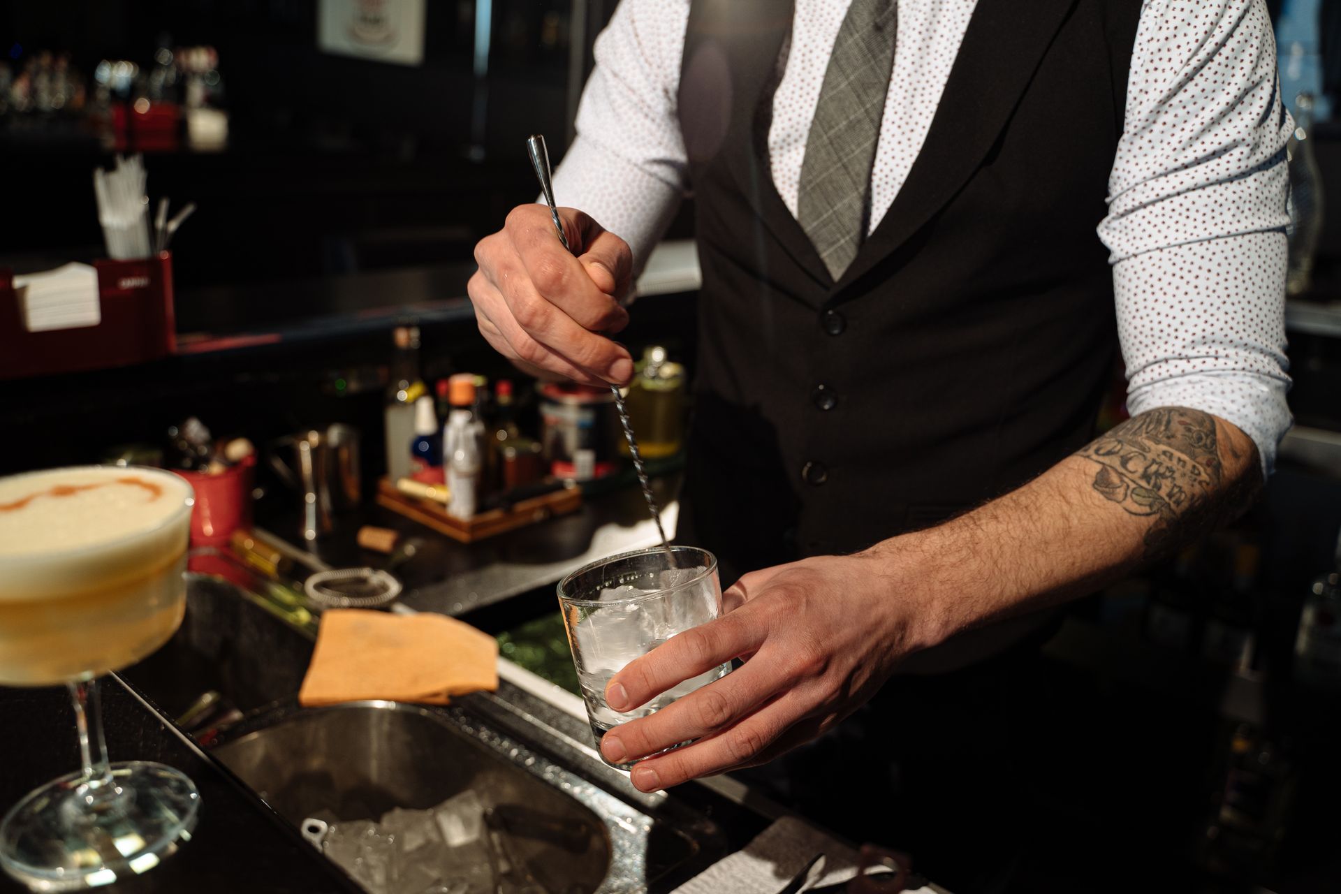Bartender in a vest stirring a cocktail at a wedding bar